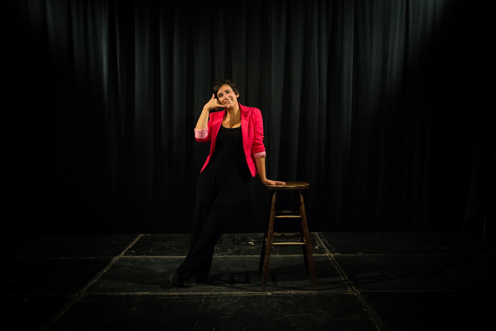 Emilie Somers, veste rose, assise sur une scène noire à côté d'un tabouret.